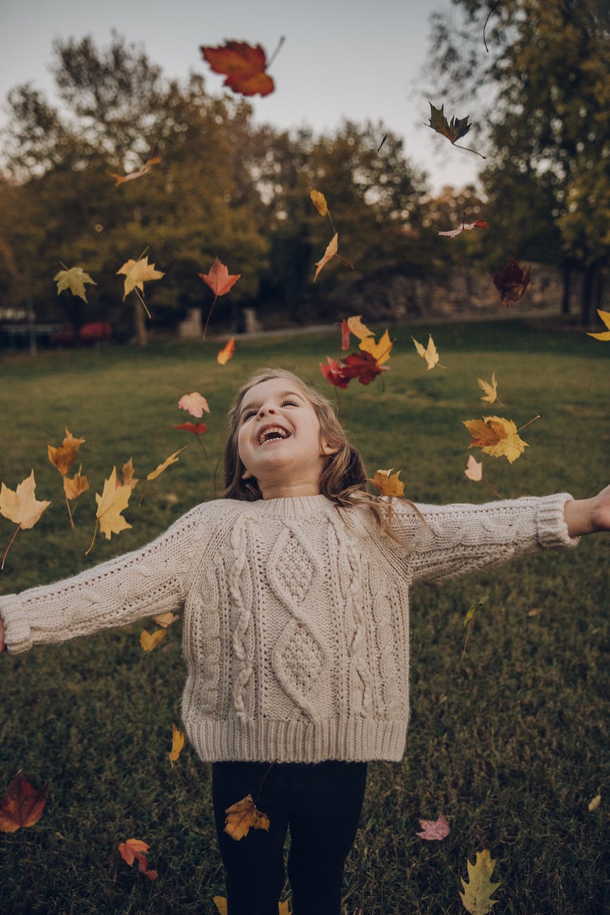 girl wearing knitted sweater standing outside with leaves falling